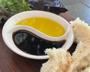 Yin and Yang Dipping Dish Favor filled with oil and vinegar on a charcuterie board with greens and bread